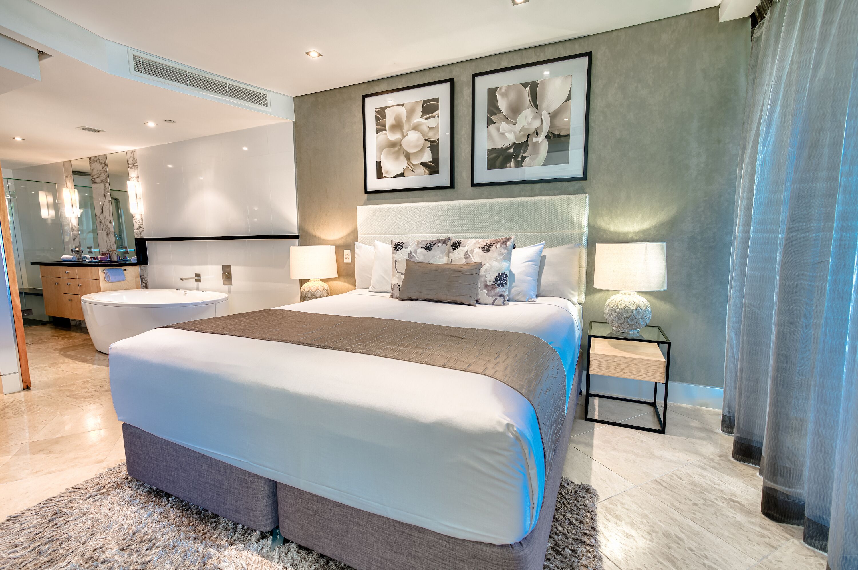 A modern bedroom with a large bed, a bathtub, and a vanity with a mirror.