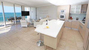 A modern kitchen with a large island, a dining area with a view of the ocean, and a living area with a flat-screen TV.