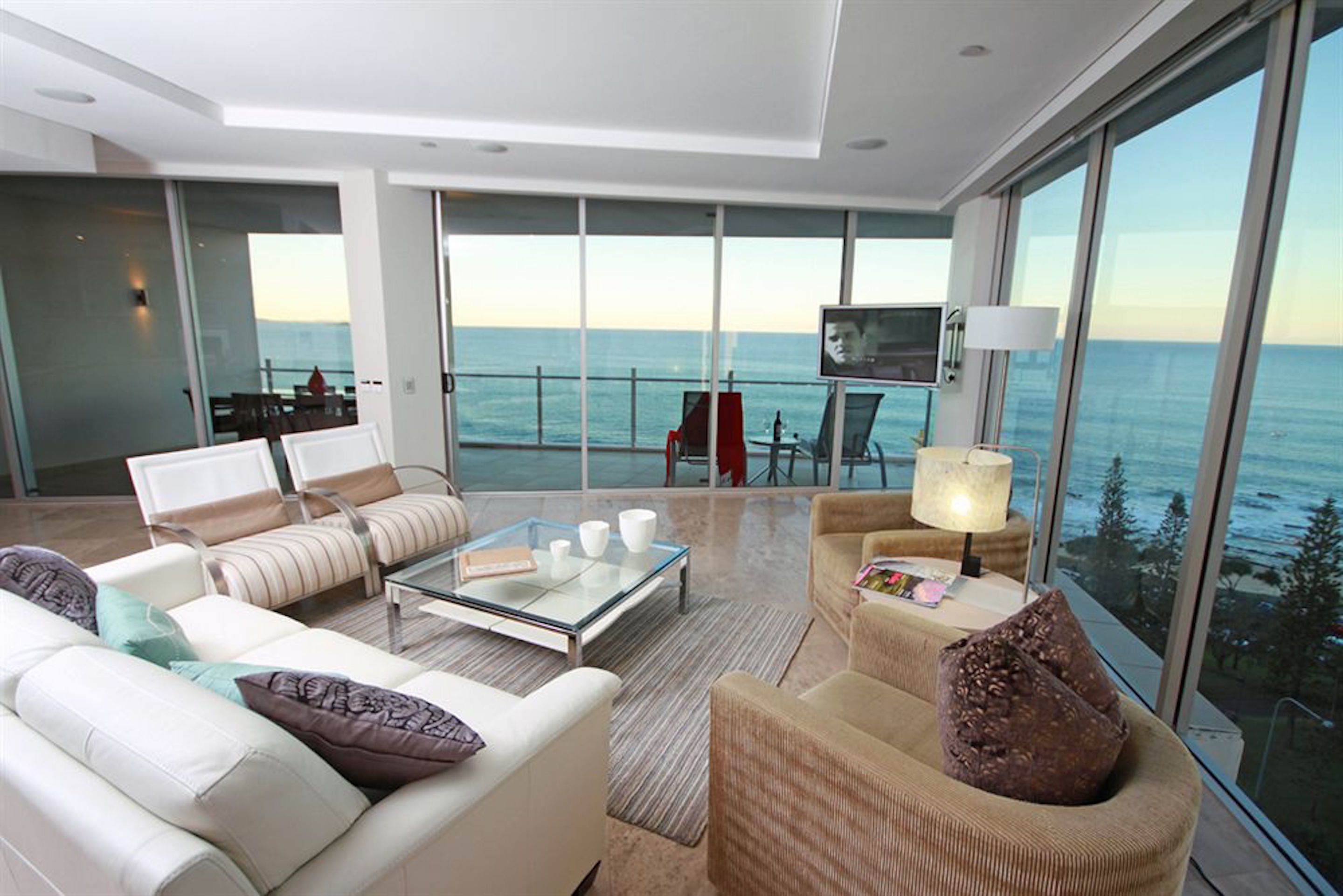 A modern living room with a glass coffee table, sofas, and armchairs, overlooking a scenic ocean view.