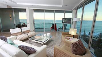 A modern living room with a glass coffee table, sofas, and armchairs, overlooking a scenic ocean view.