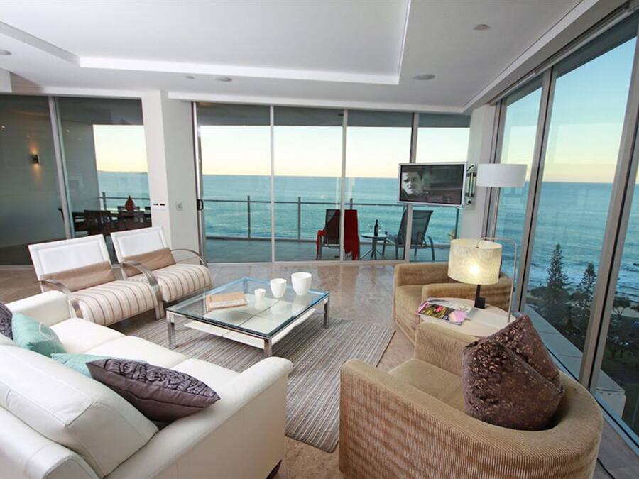 A modern living room with a glass coffee table, sofas, and armchairs, overlooking a scenic ocean view.