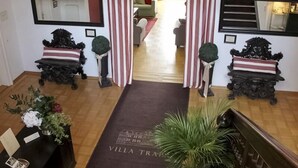 A hotel lobby with a wooden floor, a reception desk, and a red and white striped curtain. There are two ornate black sculptures on pedestals and a large mirror on the wall.