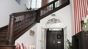 A grand staircase with a dark wooden handrail leading to a black door with a white archway above it.