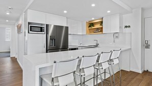 Una cocina moderna con armarios blancos, electrodomésticos de acero inoxidable y una isla central con taburetes de bar.