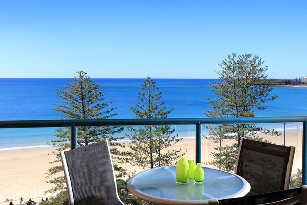 A balcony with a table and chairs, overlooking a beach and the ocean.