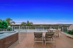 Eine Dachterrasse mit Glasgeländer, Sitzgelegenheiten im Freien und Blick auf ferne Hügel.
