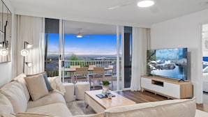 Ein modernes Wohnzimmer mit einer Couch, einem Couchtisch, einem Fernseher und einem Balkon mit Blick auf die Stadt.