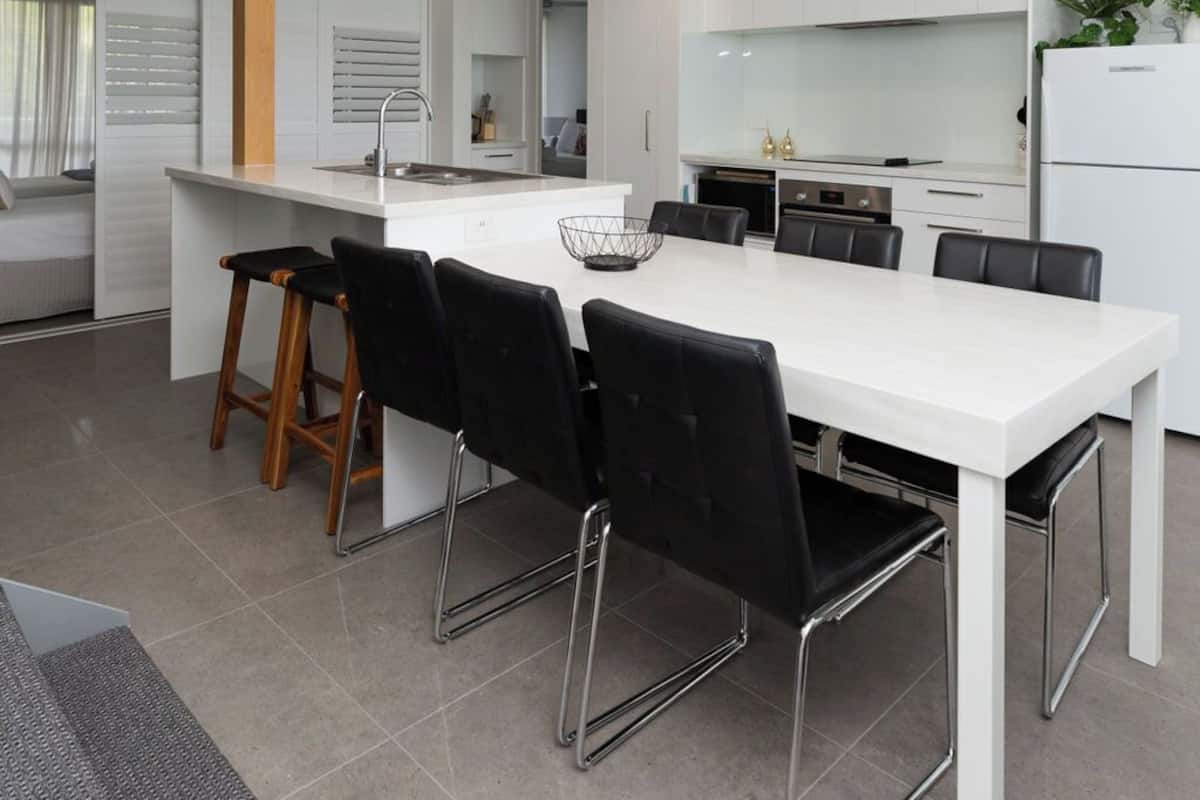 Une cuisine moderne avec des meubles blancs, un îlot central doté de sièges et un escalier menant à un niveau supérieur.