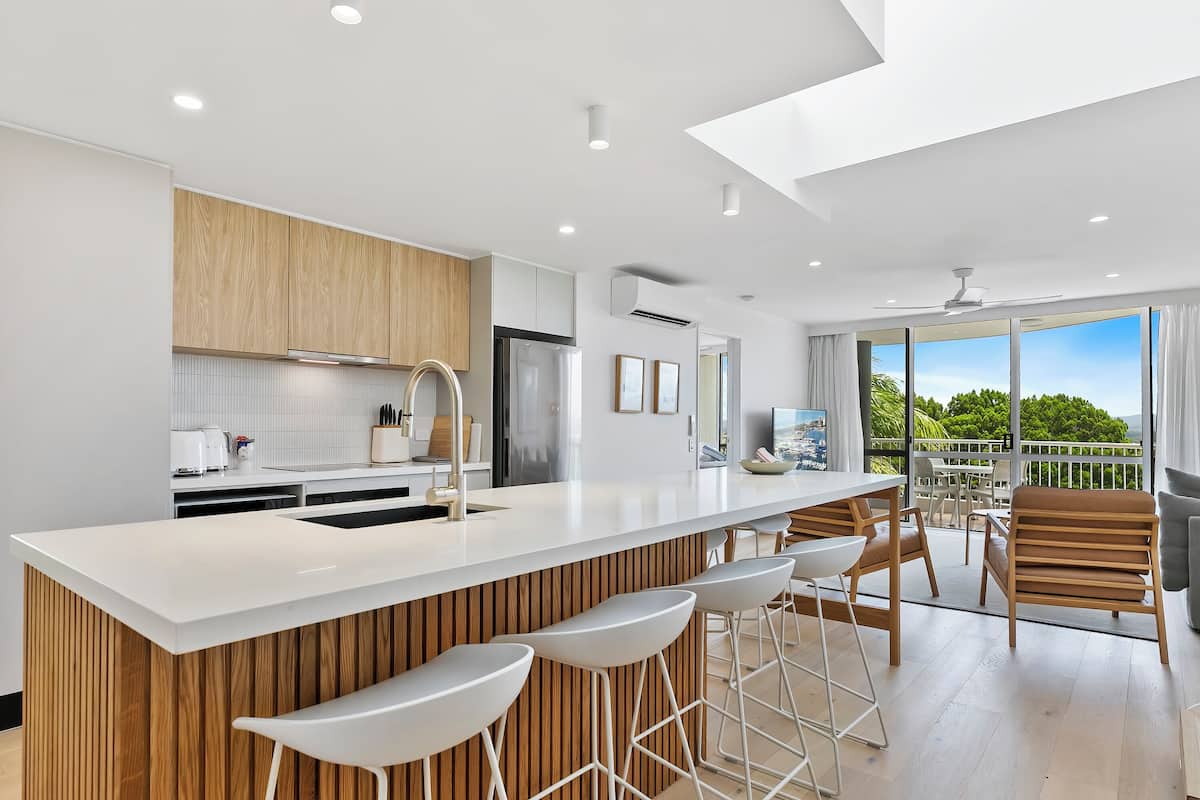 Une cuisine moderne dotée d’un grand îlot central, de touches de bois et offrant une vue sur l’extérieur.