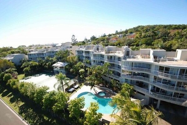 Ein Hotel mit Schwimmbad, umgeben von üppiger Vegetation und mehreren Balkonen.
