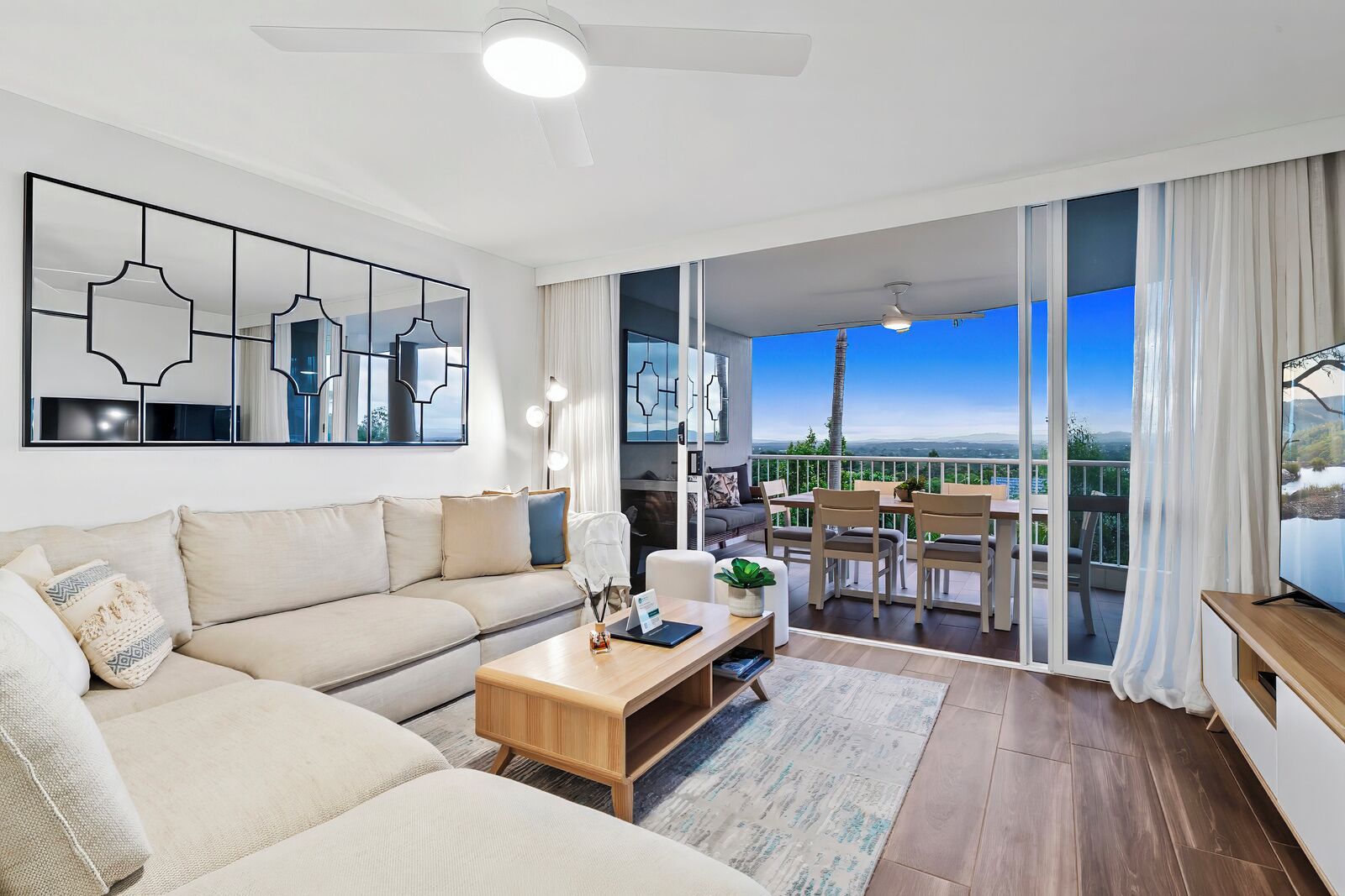 Een moderne woonkamer met een bank, salontafel en een eethoek. Er is een balkon met uitzicht op het landschap.