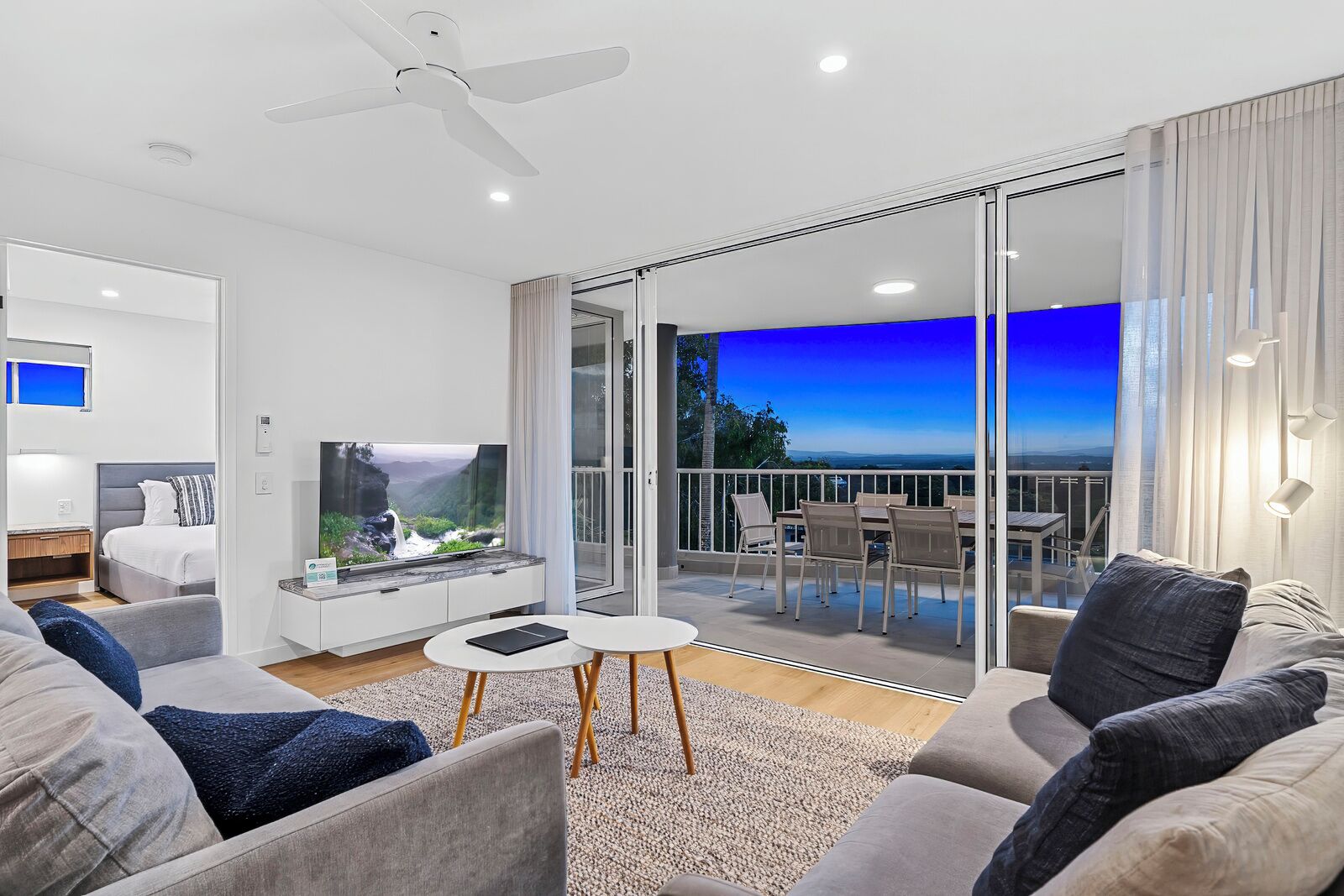 Una sala de estar moderna con una televisión de pantalla plana, un sofá, una mesa de centro y un balcón con vistas al océano.