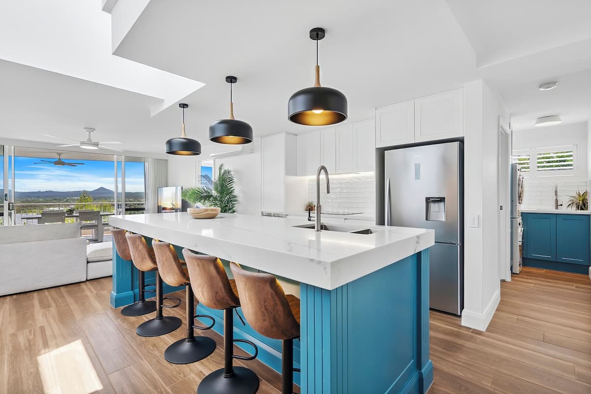 Une cuisine moderne dotée d’un îlot central, de tabourets de bar, de luminaires suspendus et offrant une vue sur l’extérieur.