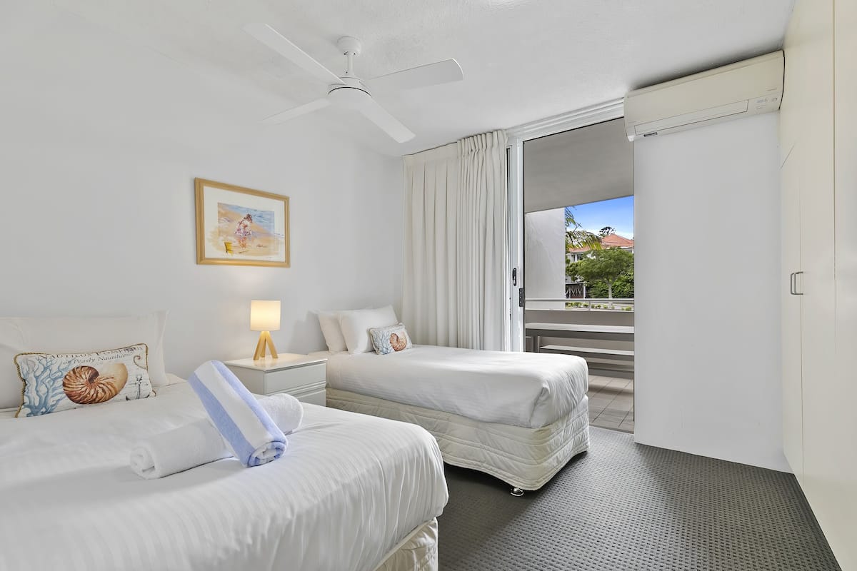 Une chambre d’hôtel avec deux lits, un ventilateur de plafond, un tableau et une vue sur l’extérieur.