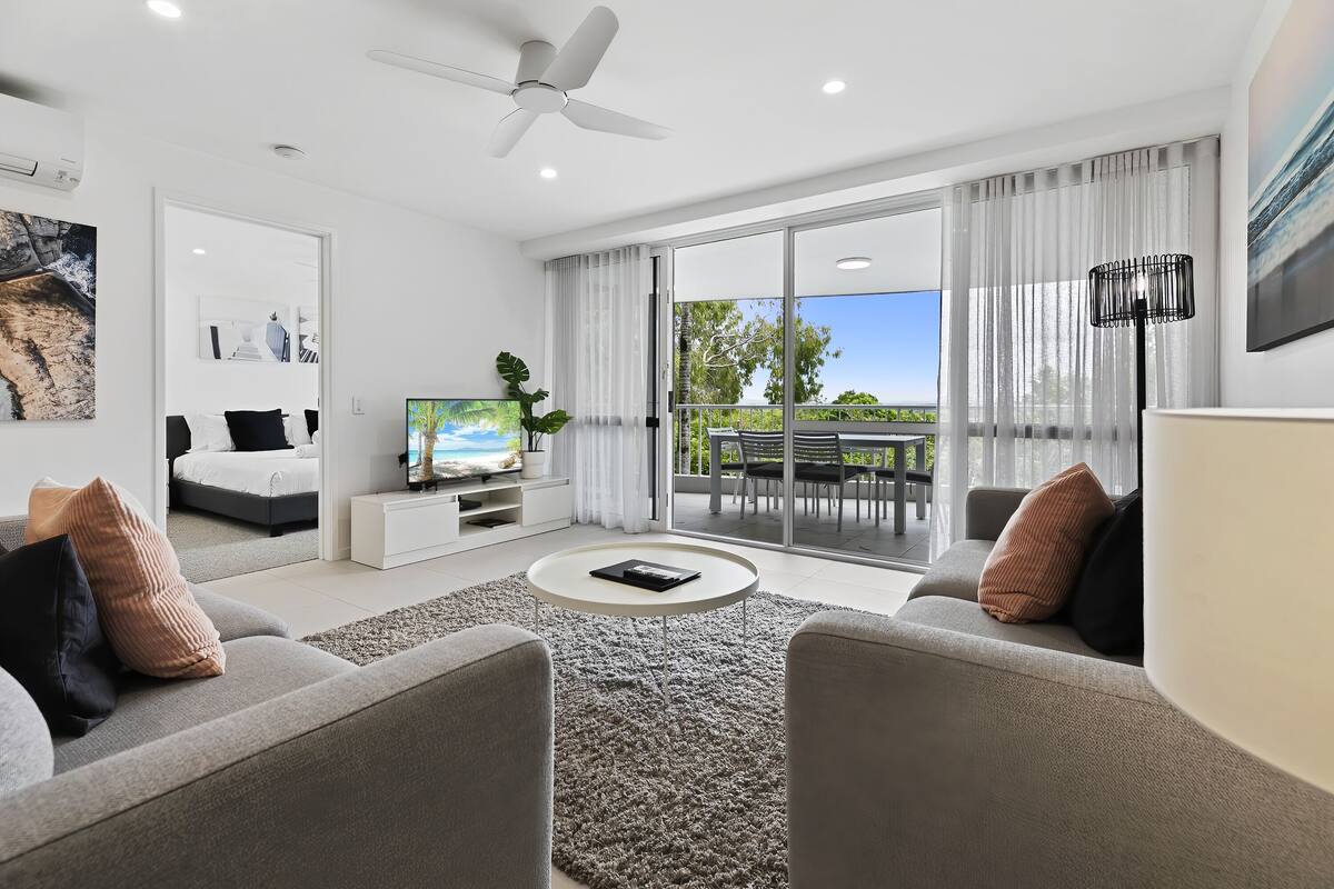 Un salon moderne avec un canapé, une table basse, un téléviseur et un balcon offrant une vue agréable.