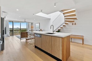A modern kitchen with a central island, wooden flooring, and a view of the outdoors.