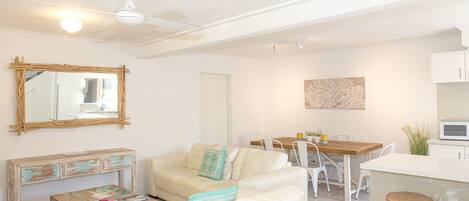 Una sala de estar moderna con un sofá blanco, una mesa de centro de madera y una zona de comedor con una mesa de madera y sillas blancas.