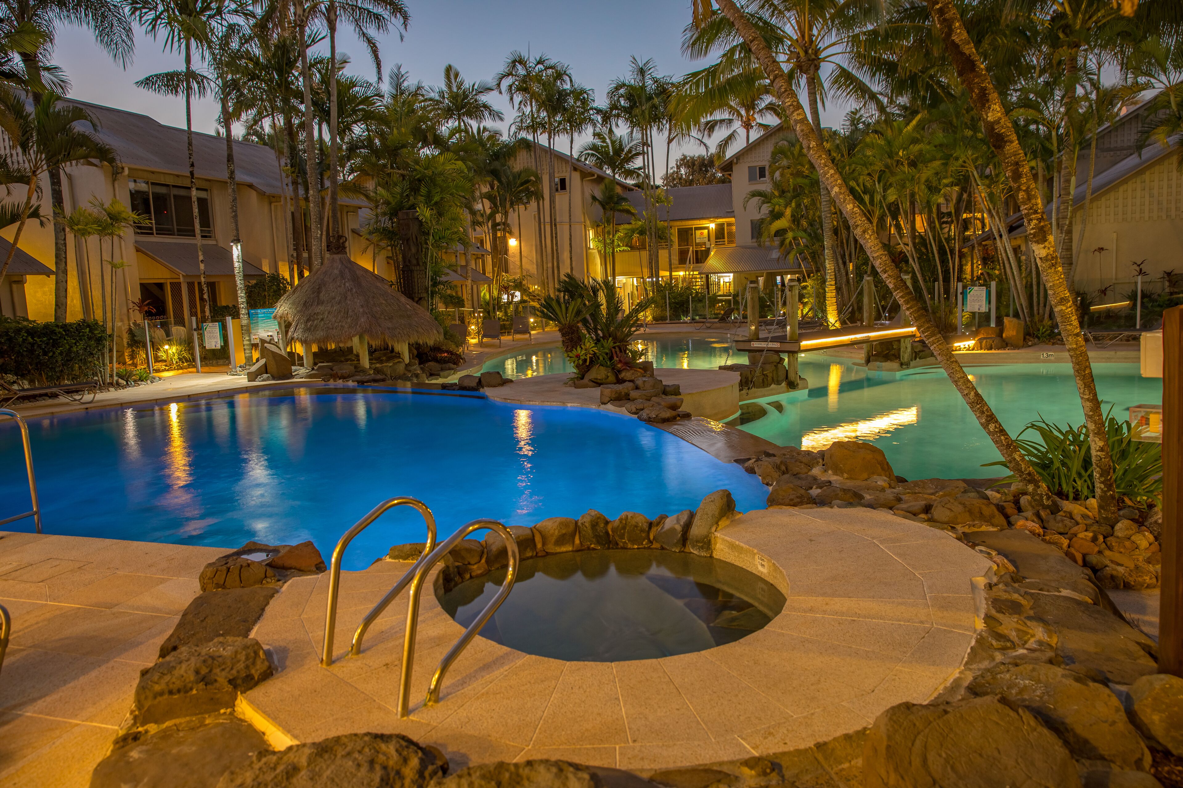 Área de piscina de resort com hidromassagem, espreguiçadeiras e palmeiras.