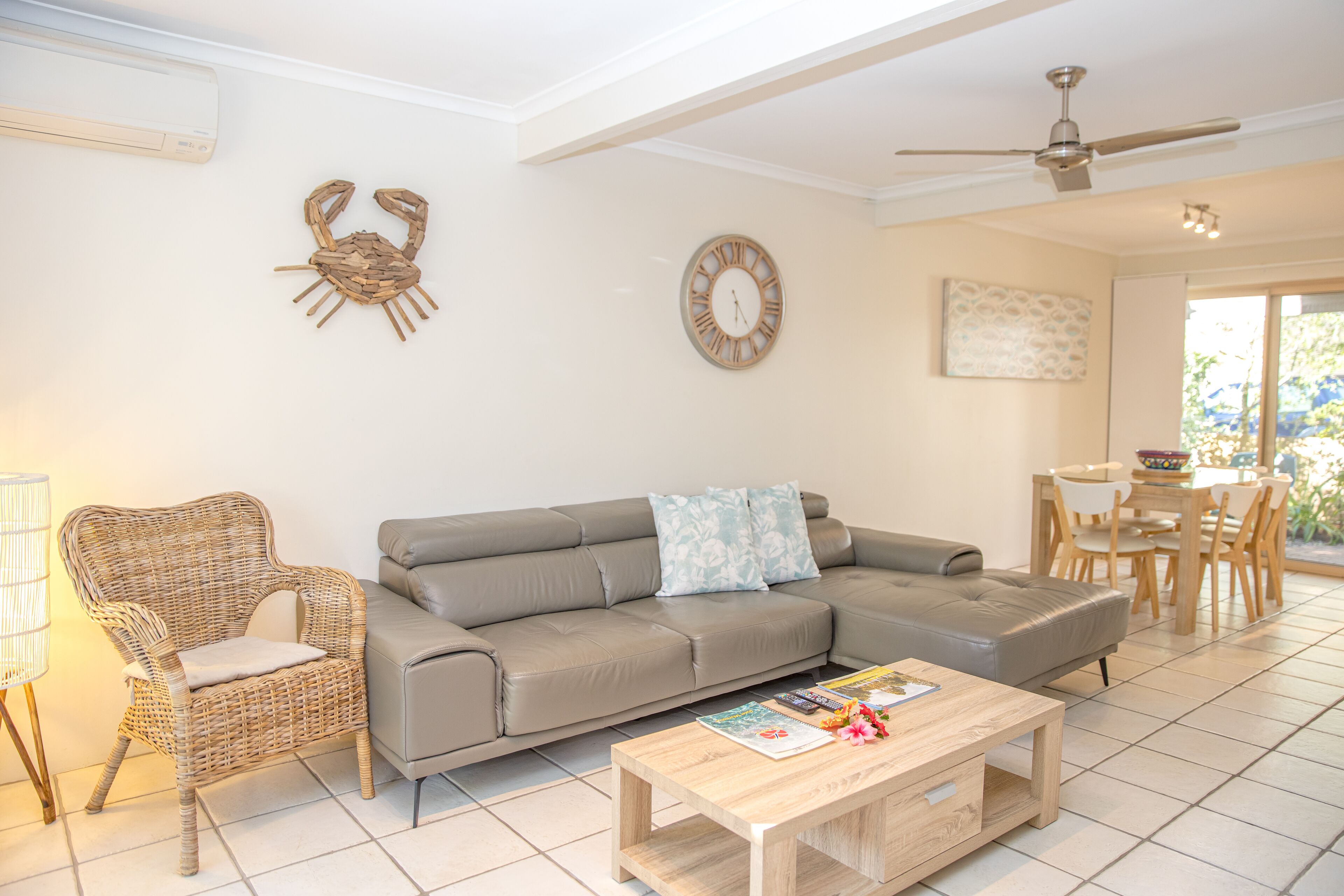 A living room with a sofa, a wooden coffee table, a wicker chair, a wall clock, and a ceiling fan.