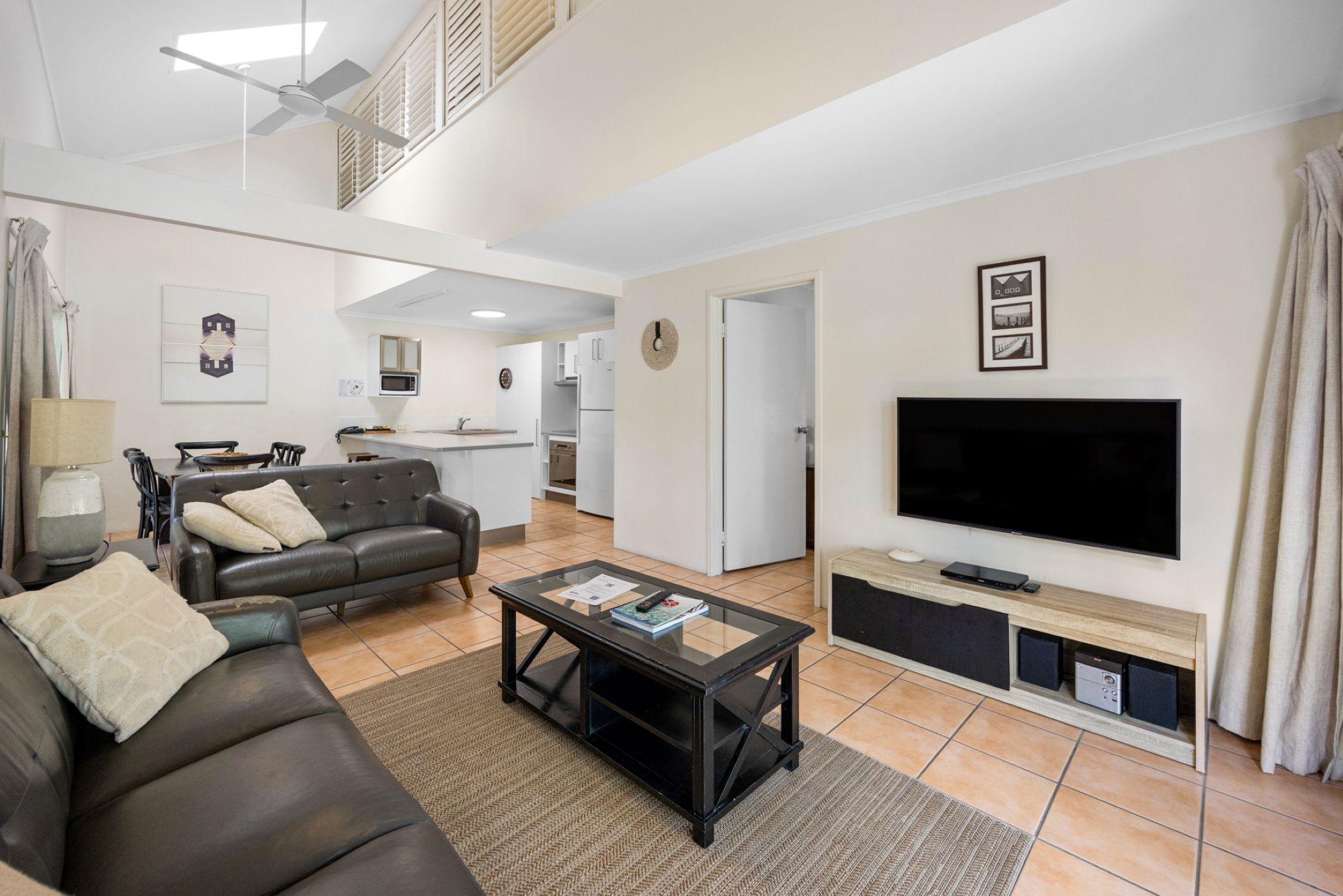 A living room with a sofa, coffee table, TV, and kitchen in the background.