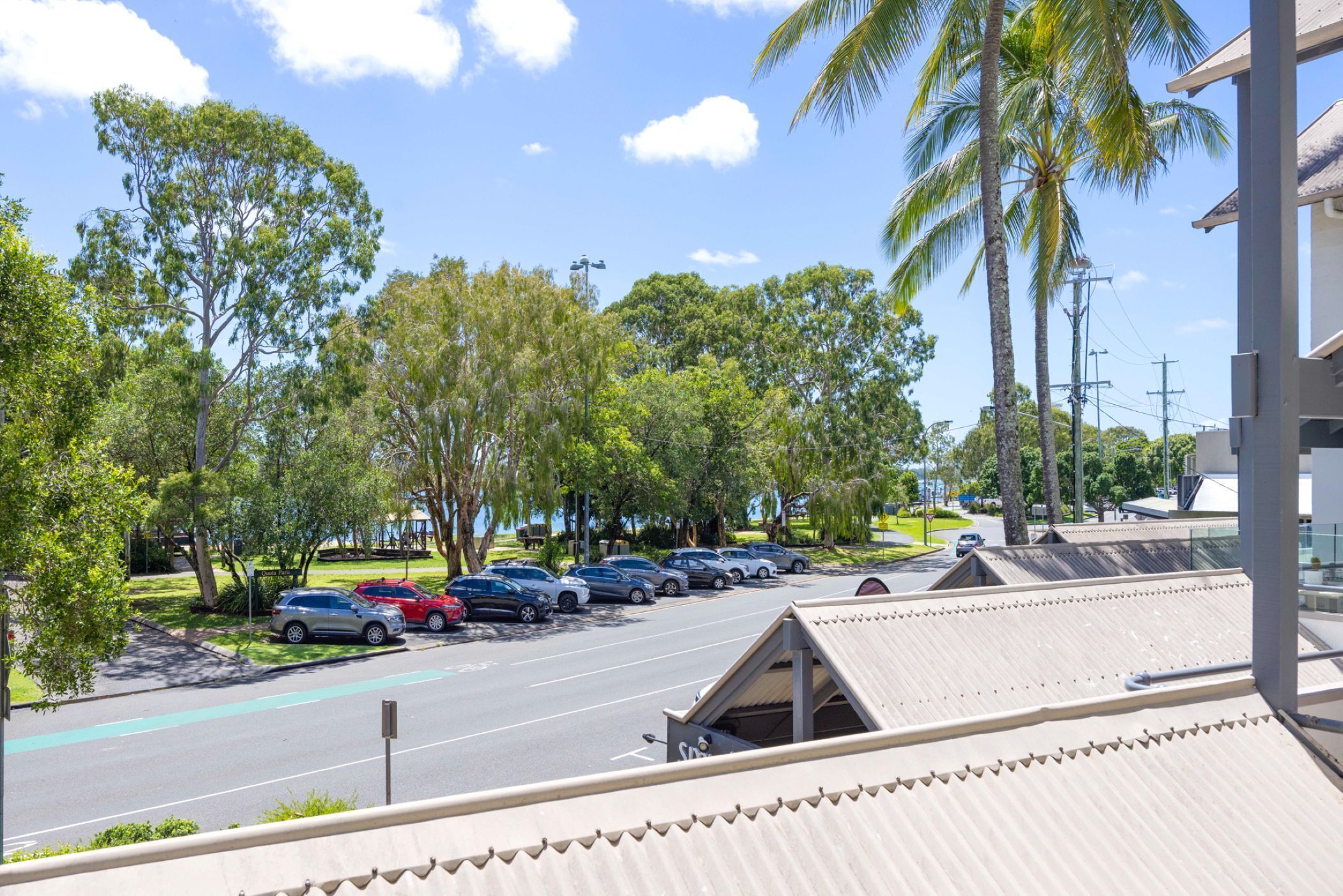 A parking lot with several cars, a building with a sloped roof, and palm trees.