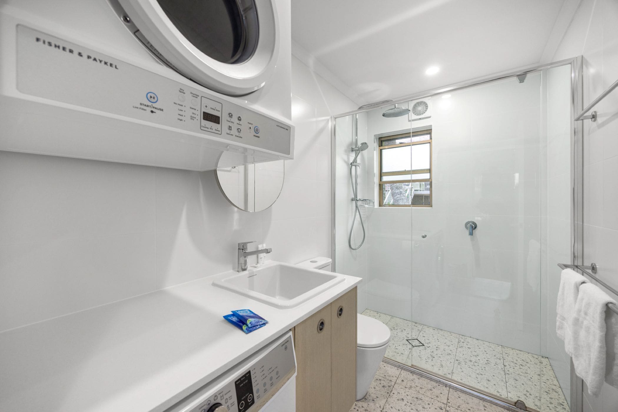 A modern bathroom with a built-in washing machine, a sink, a toilet, and a glass-enclosed shower area.