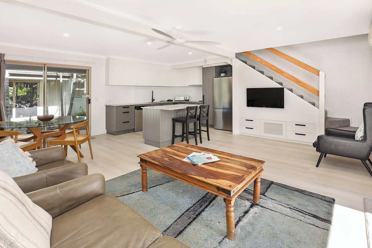 A modern living room with a glass dining table, leather sofa, and a wooden coffee table.