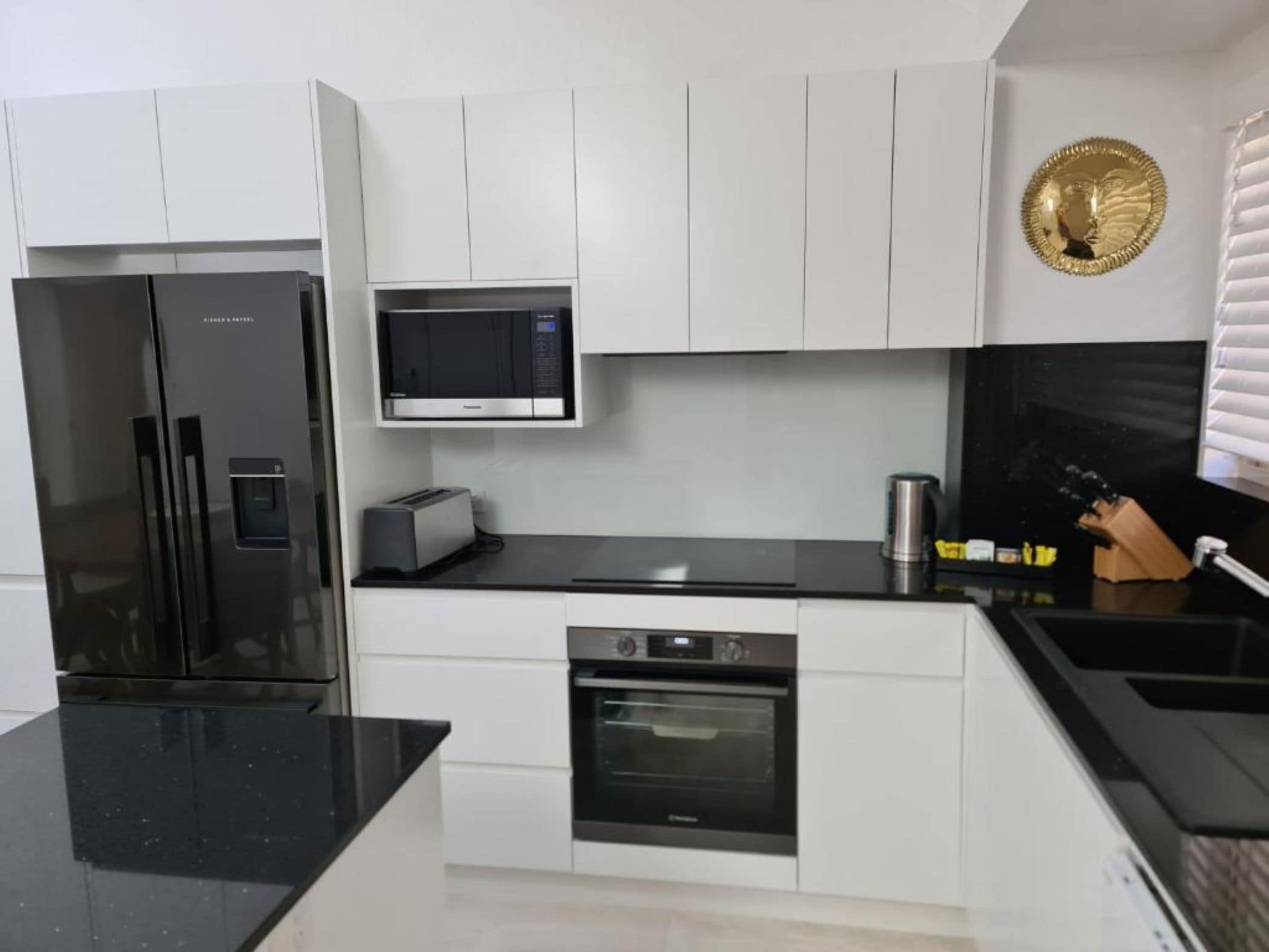A modern kitchen with a refrigerator, microwave, toaster, oven, and black countertops.