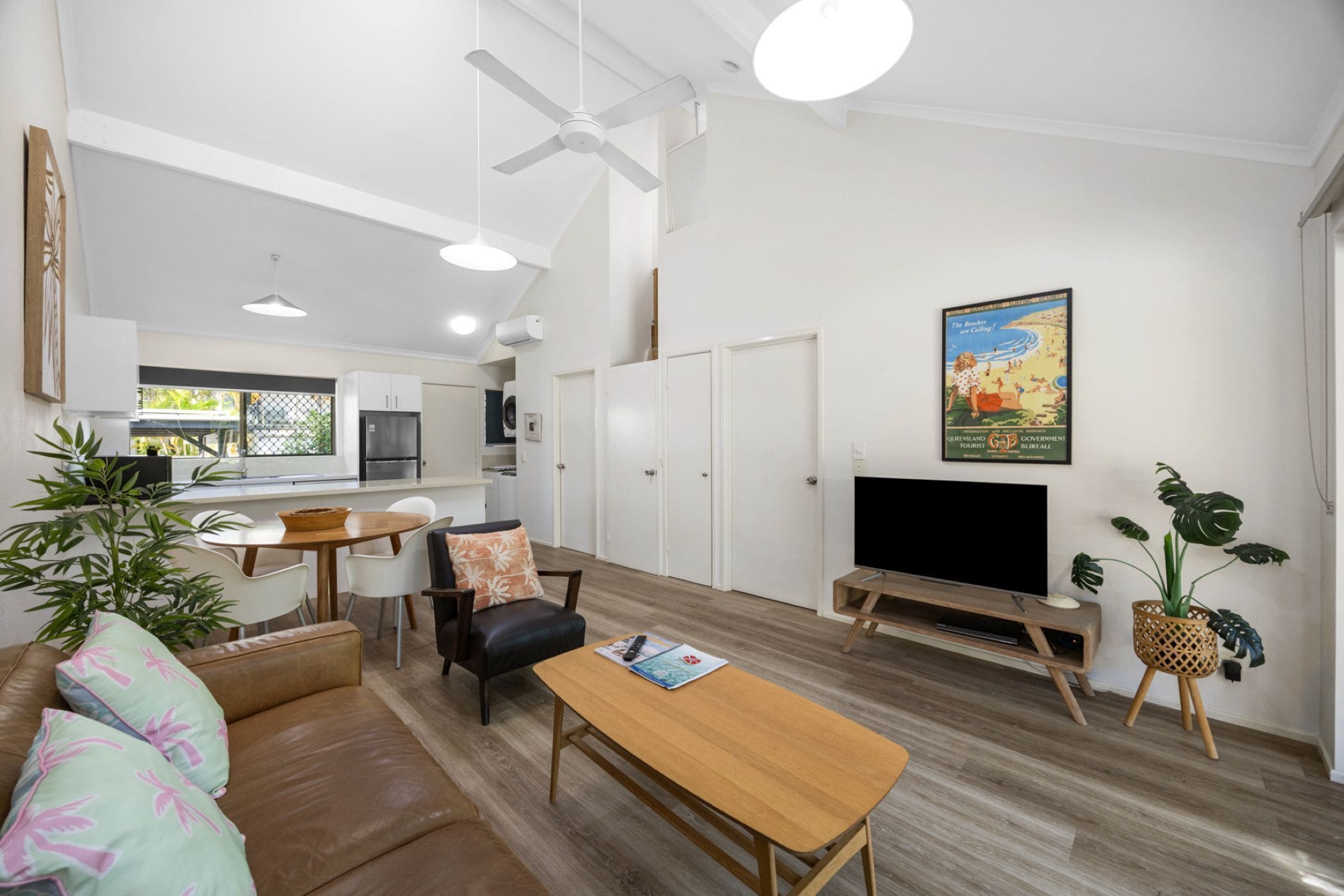 A modern living room with a sofa, coffee table, TV, and a dining area with chairs and a table.