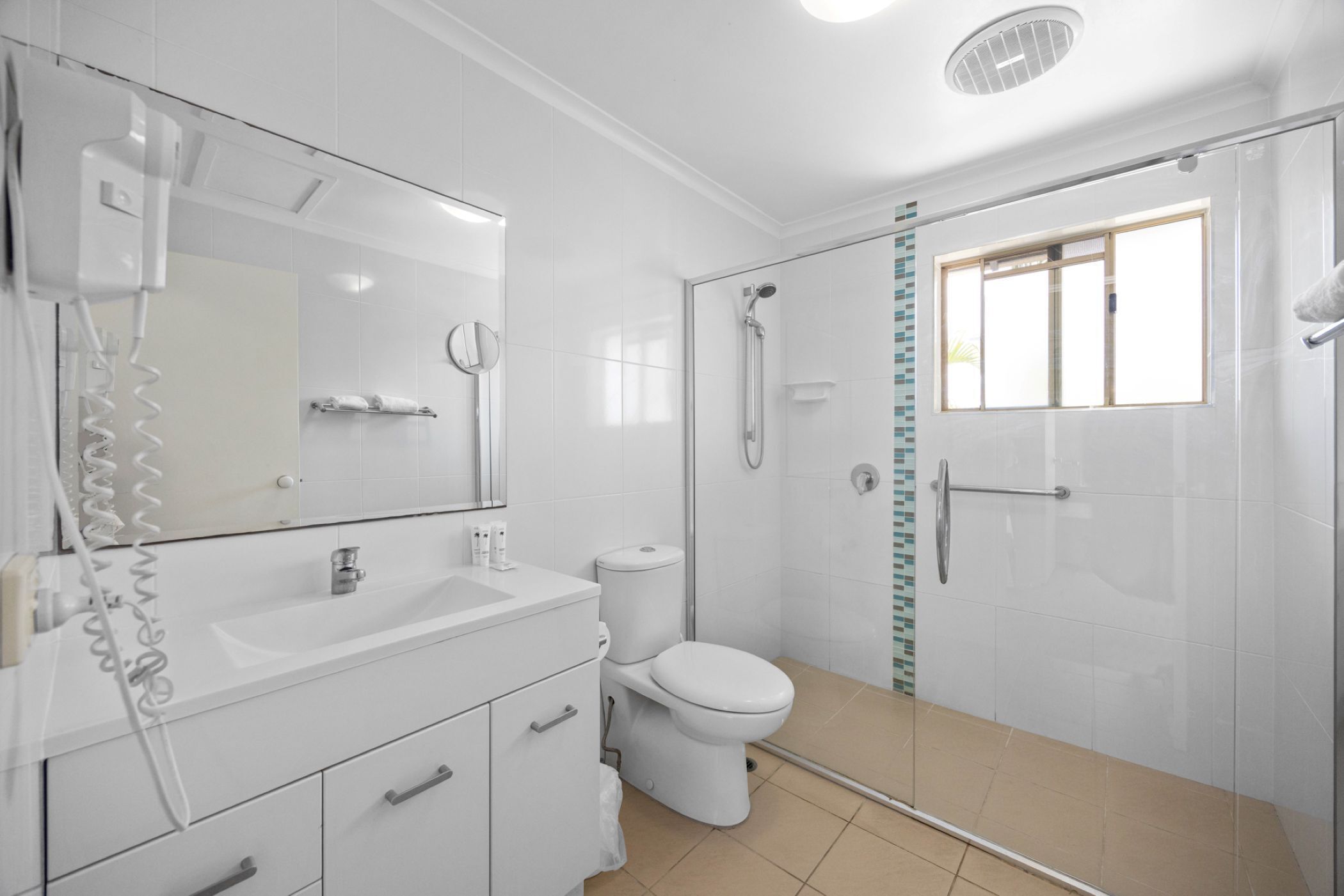 Une salle de bain avec un lavabo, des toilettes et une douche, le tout de couleur blanche.