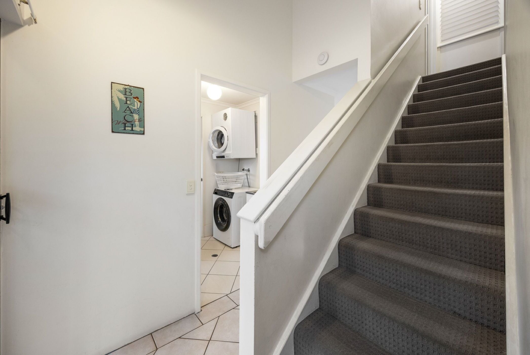 Una escalera que lleva a un área de lavandería con lavadora y secadora, una puerta con luz y un cartel en la pared.