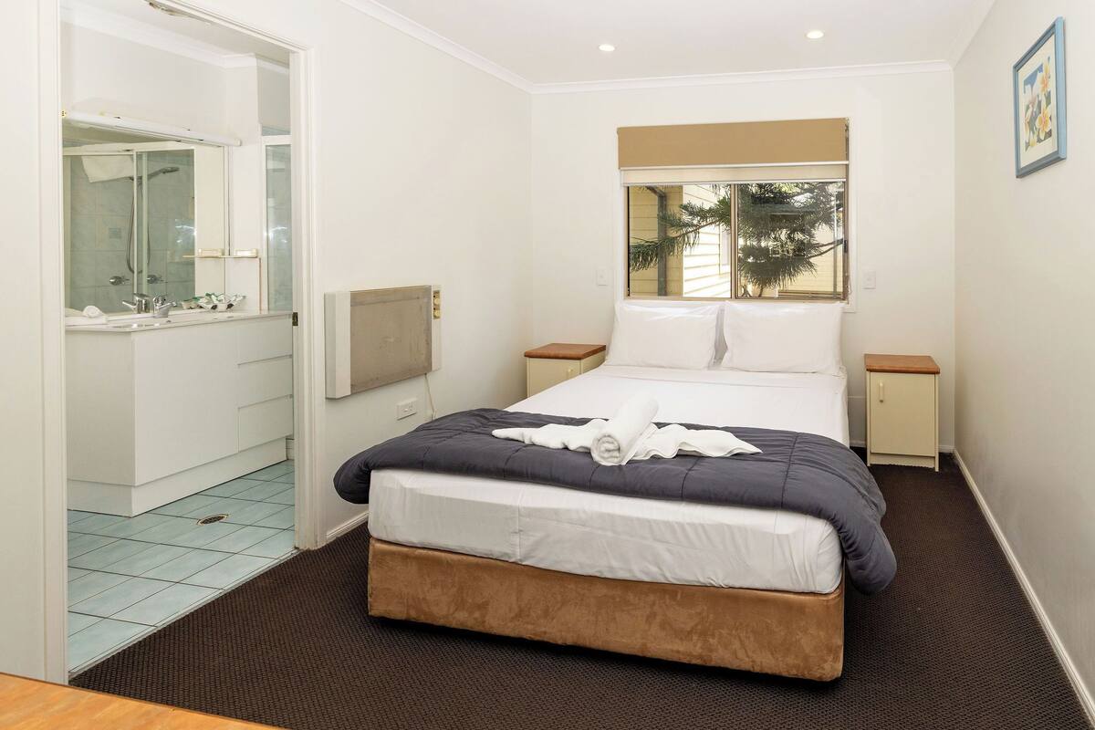 Een slaapkamer met een bed, nachtkastjes, een raam met uitzicht, een badkamer met spiegel en douche.