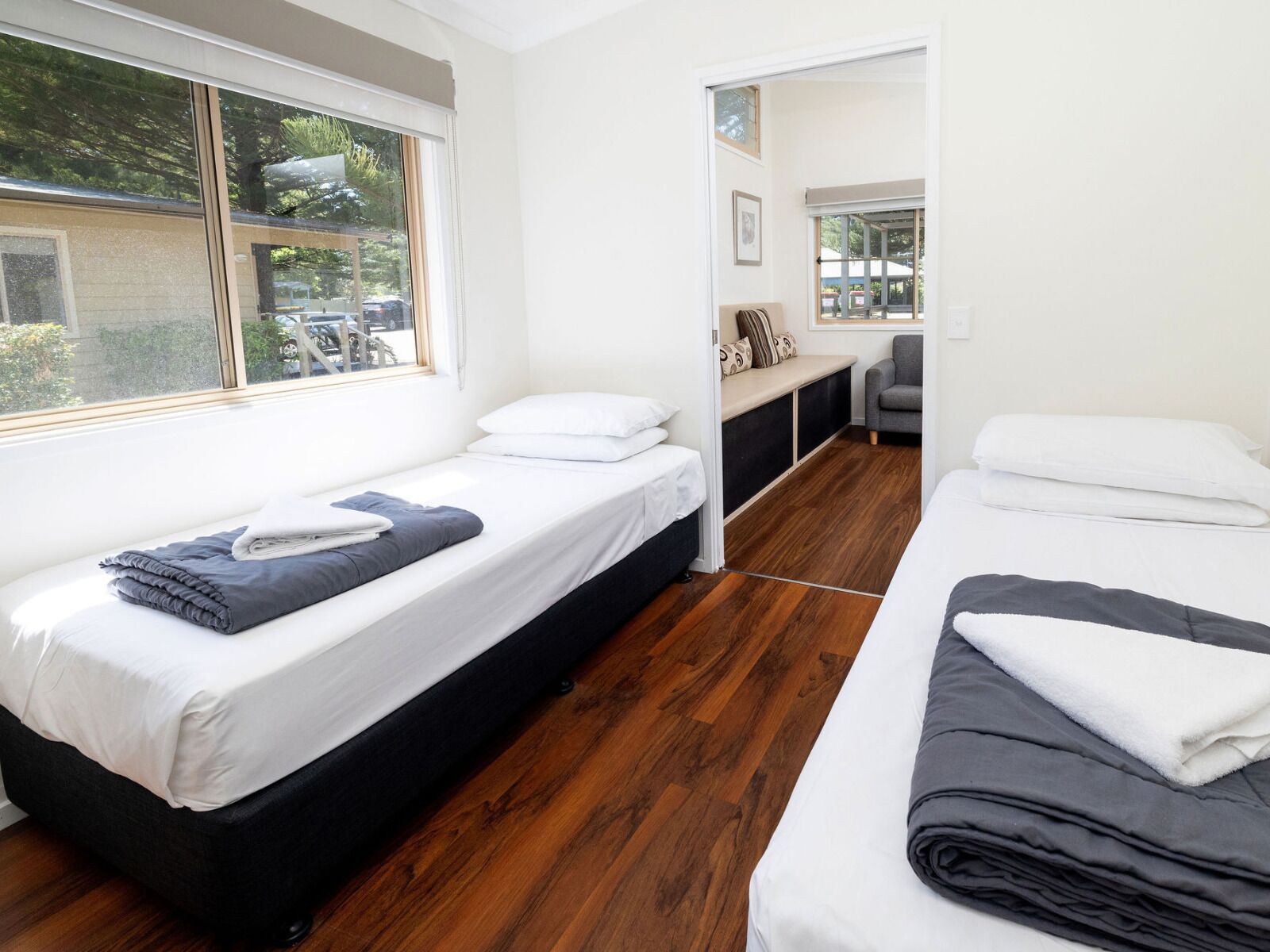Quarto moderno e compacto com duas camas de solteiro, um pequeno espaço de estar e uma grande janela com vista para o exterior.