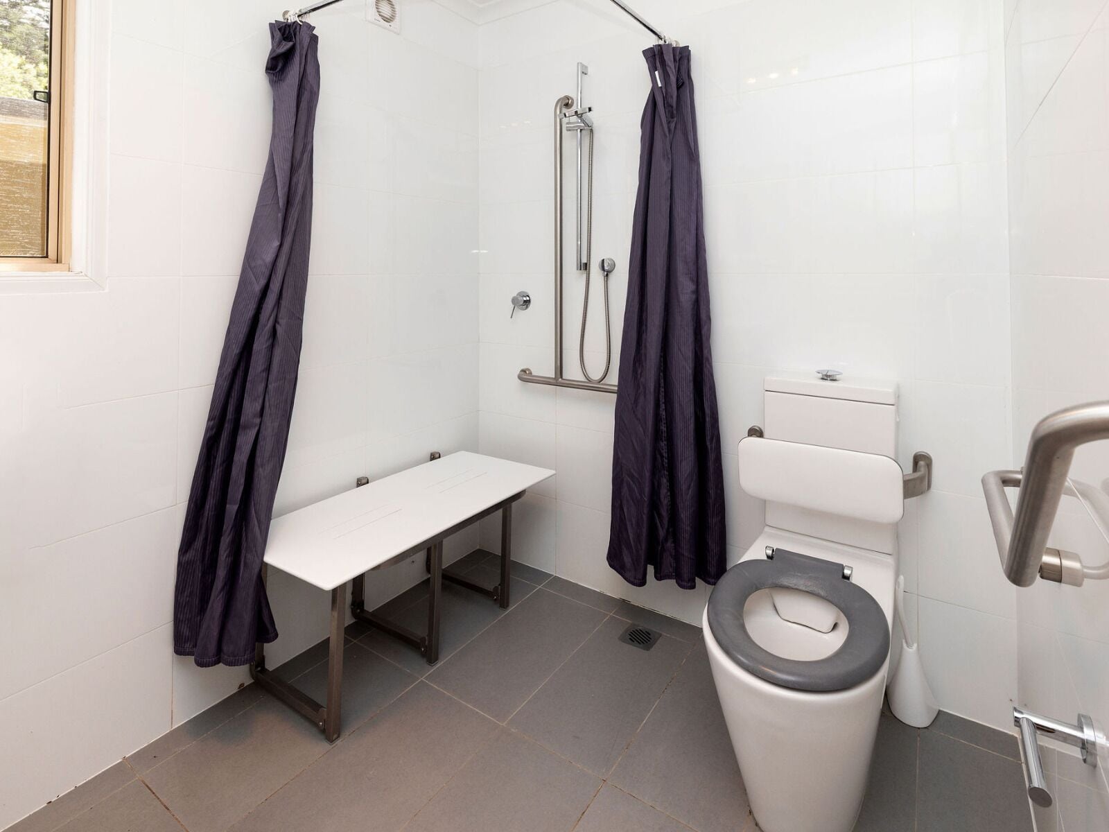 A modern bathroom with a shower, toilet, and bench.