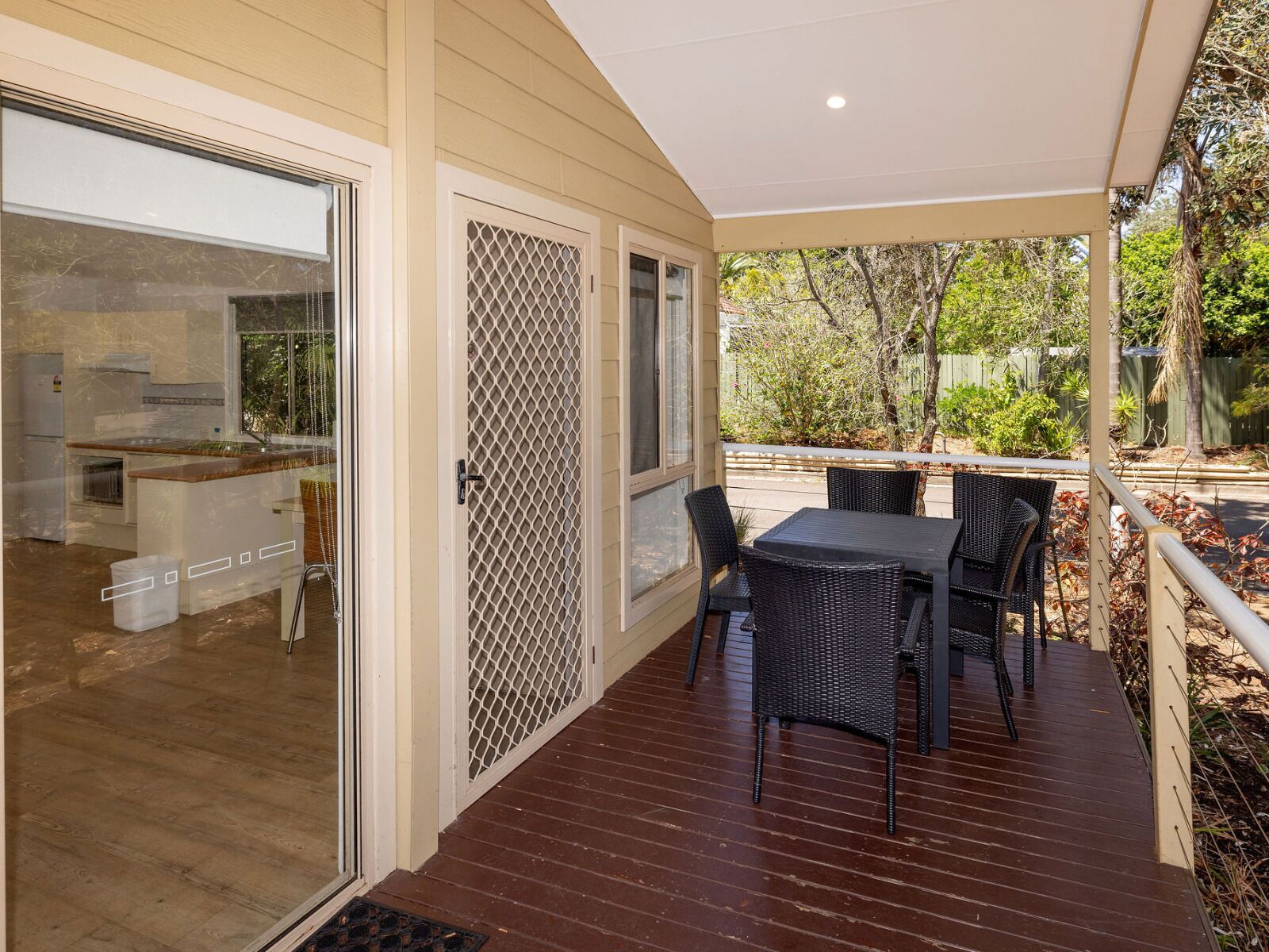 A covered patio with a dining table and chairs, a sliding glass door leading to a kitchen, and a view of the surrounding greenery.
