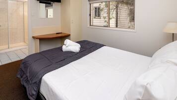 A hotel room with a bed, a bedside table, a TV mounted on the wall, a window with a view of the outside, and a shower area.