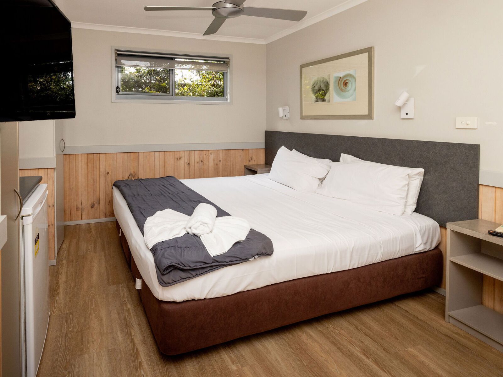 Quarto com cama, ventoinha no teto, janela e televisão na parede.