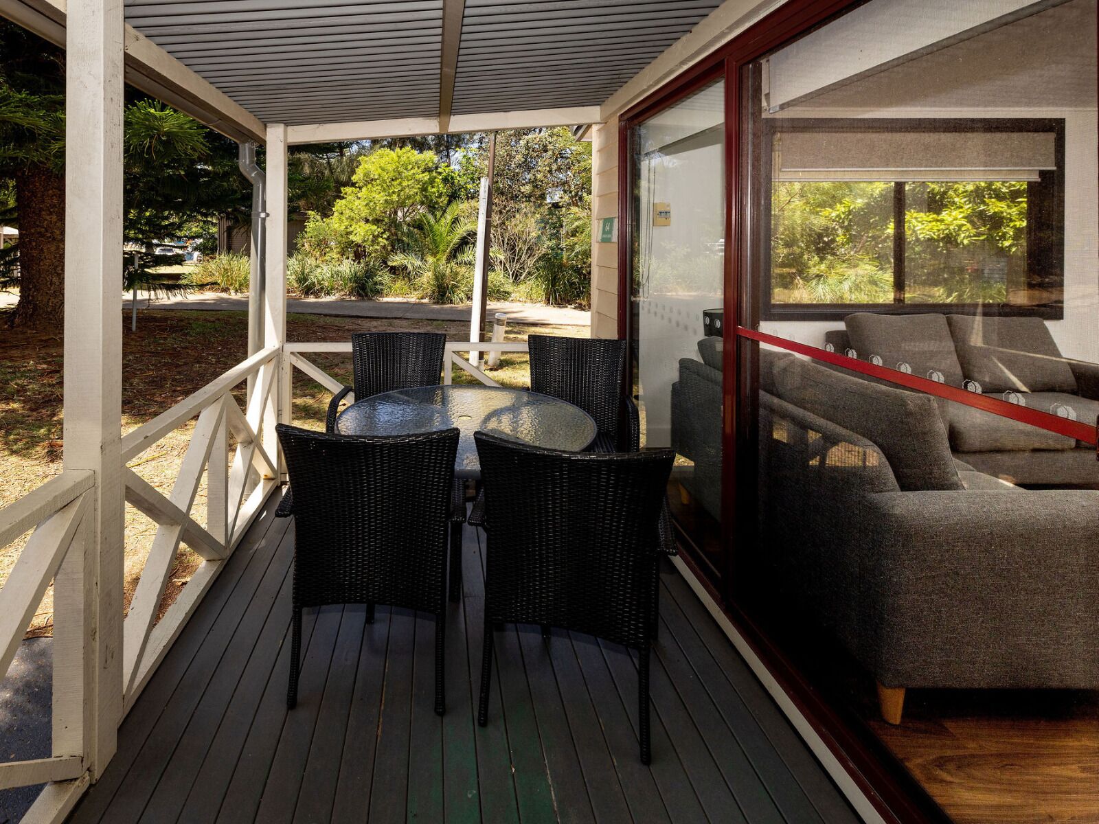 A covered outdoor area with a table and chairs, a sofa, and a view of the surrounding greenery.