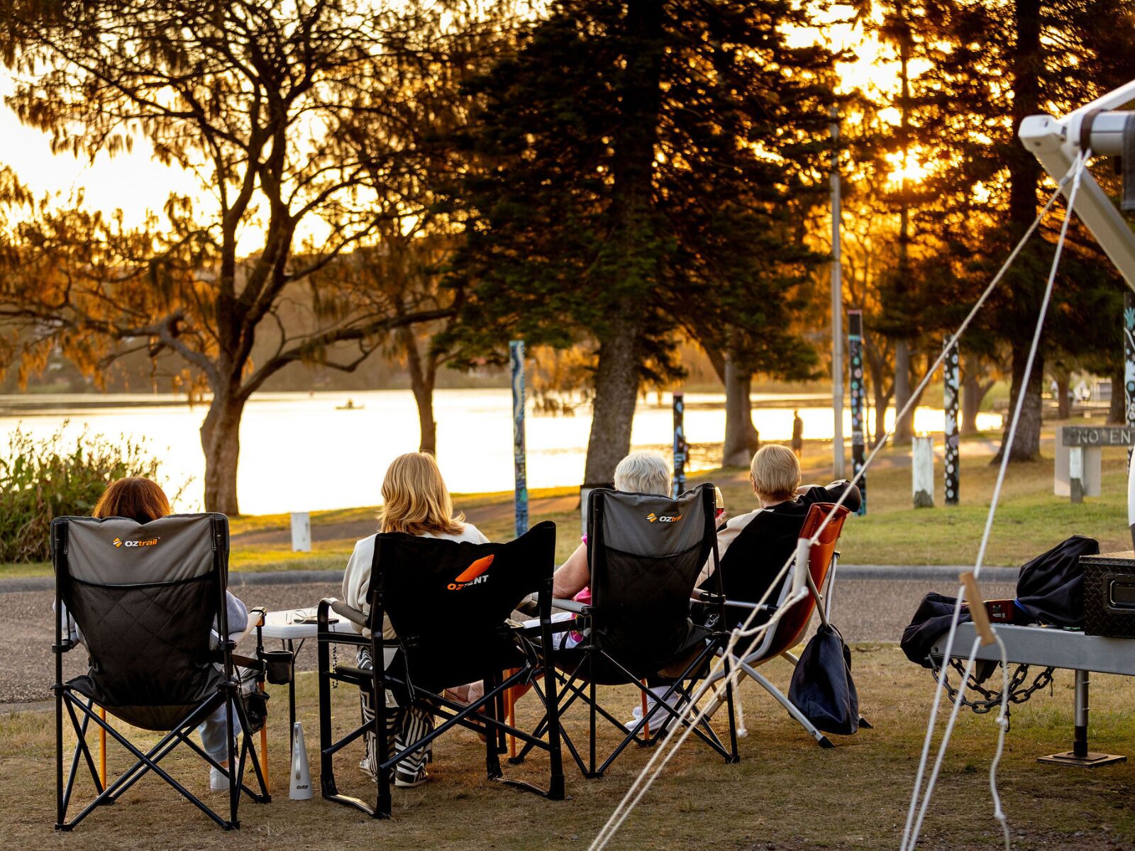 Three people seated in Oztrail chairs facing a lake.