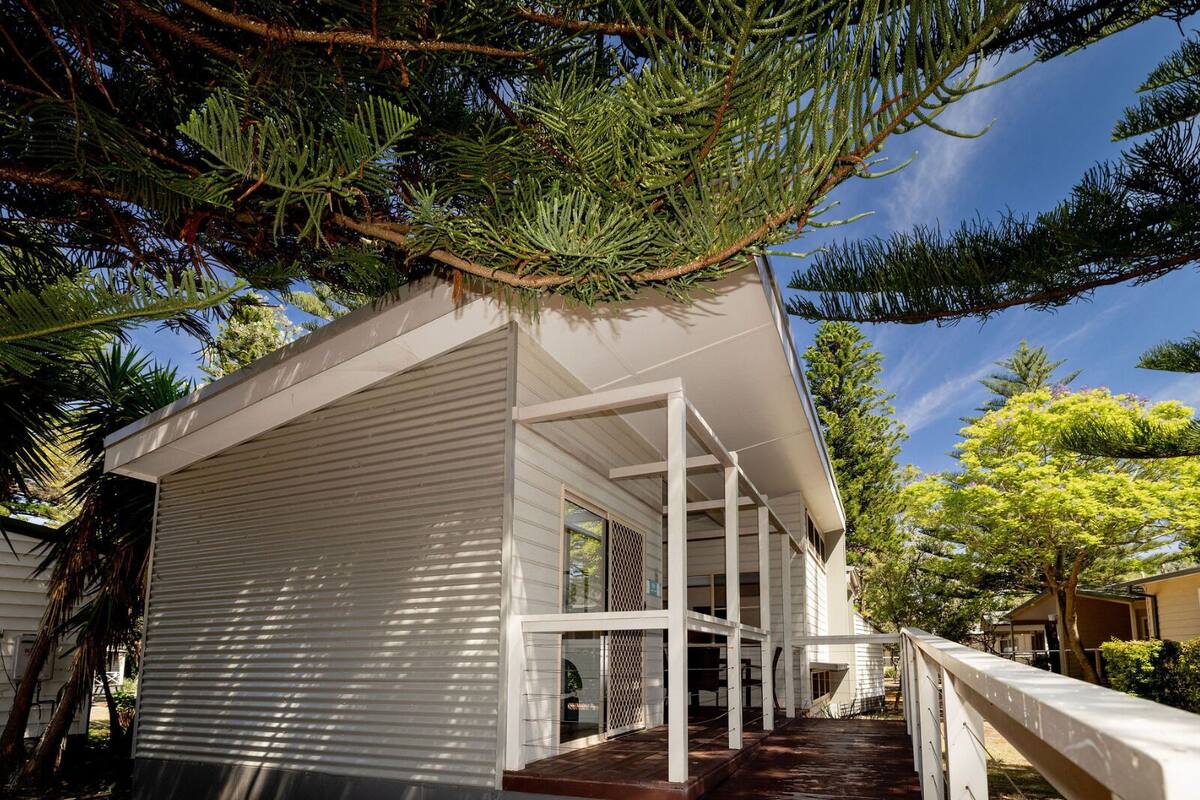 Een modern huis met een overdekte veranda, een omheind erf en een grote boom op de achtergrond.