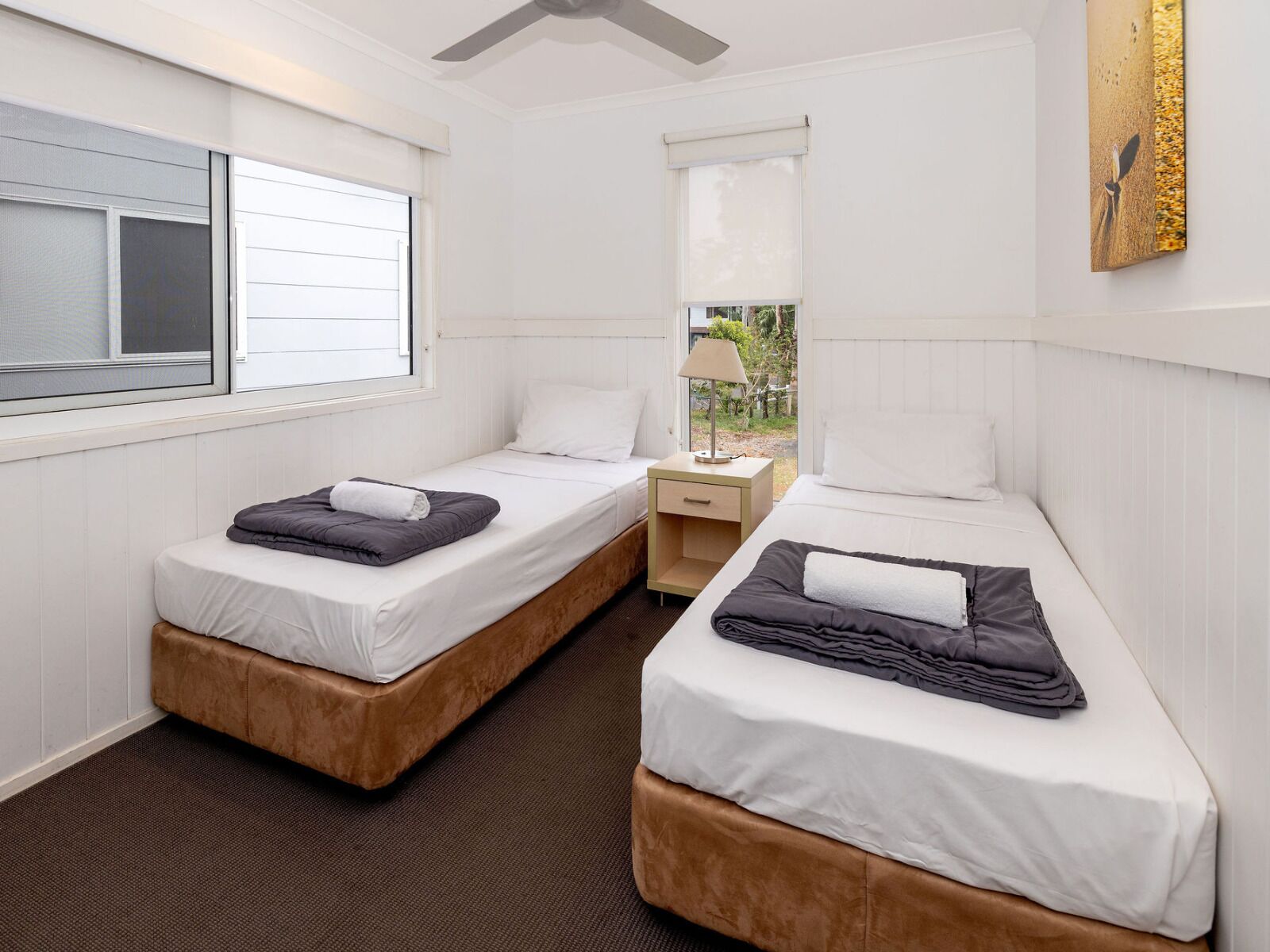 Une chambre d’hôtel avec deux lits, une fenêtre, un ventilateur de plafond et une petite table avec une lampe.