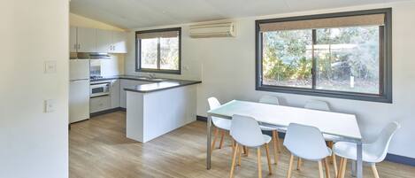 A modern kitchen with white cabinets, a central island, and a dining area with a white table and chairs.