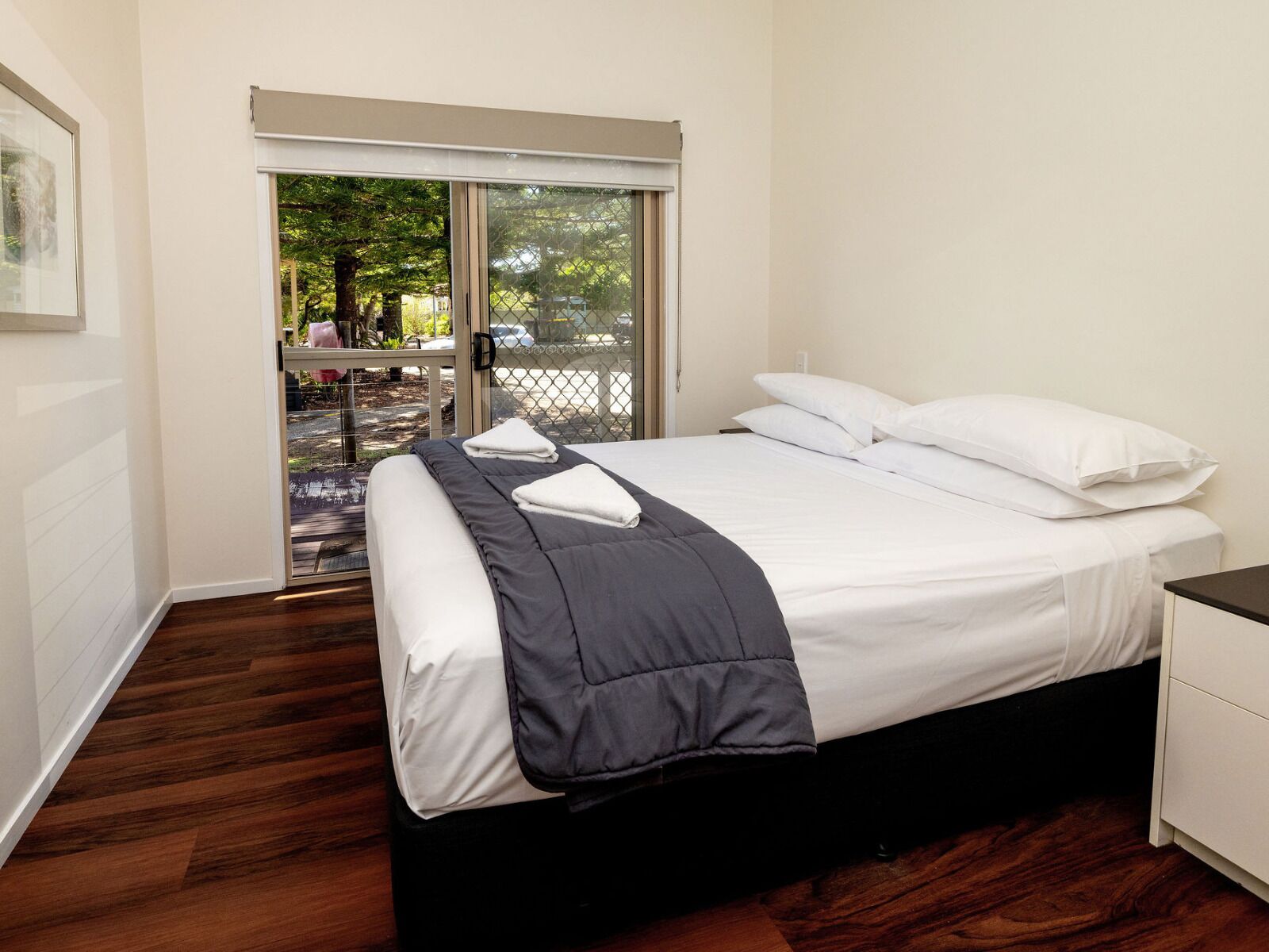 Une chambre à coucher comprenant un lit, une table de chevet, une fenêtre donnant sur l’extérieur et une porte.
