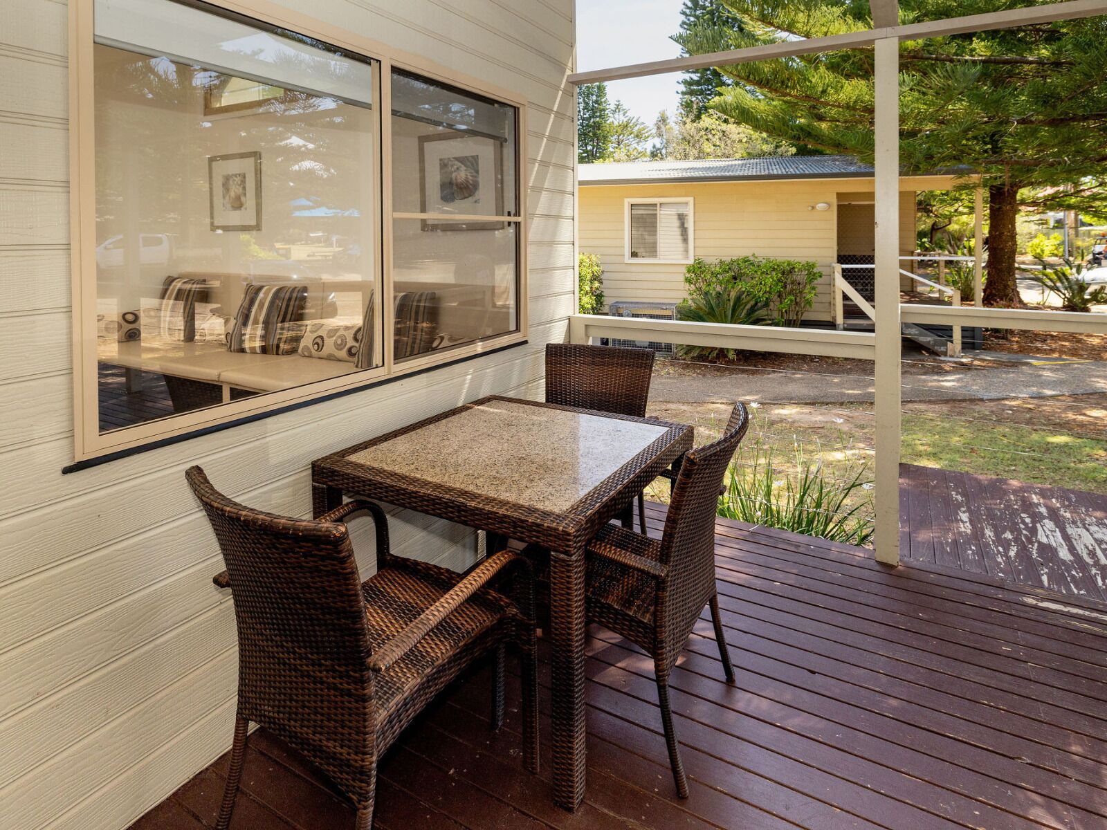 A covered patio with a table and chairs, a window with a view of the house, and a wooden deck.