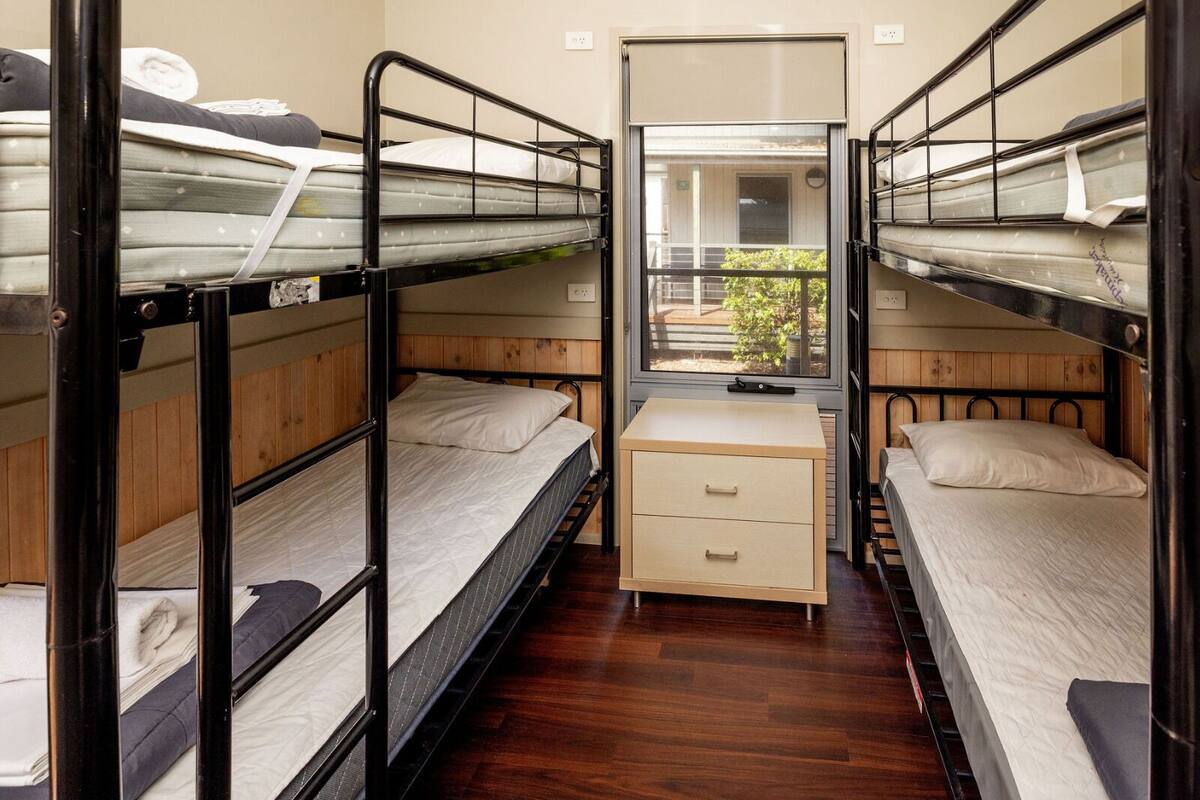 Een kleine kamer met stapelbedden, een bureau en een raam met uitzicht op de omgeving.