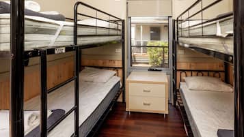 A compact room with bunk beds, a small desk, and a window providing a view of the outdoors.