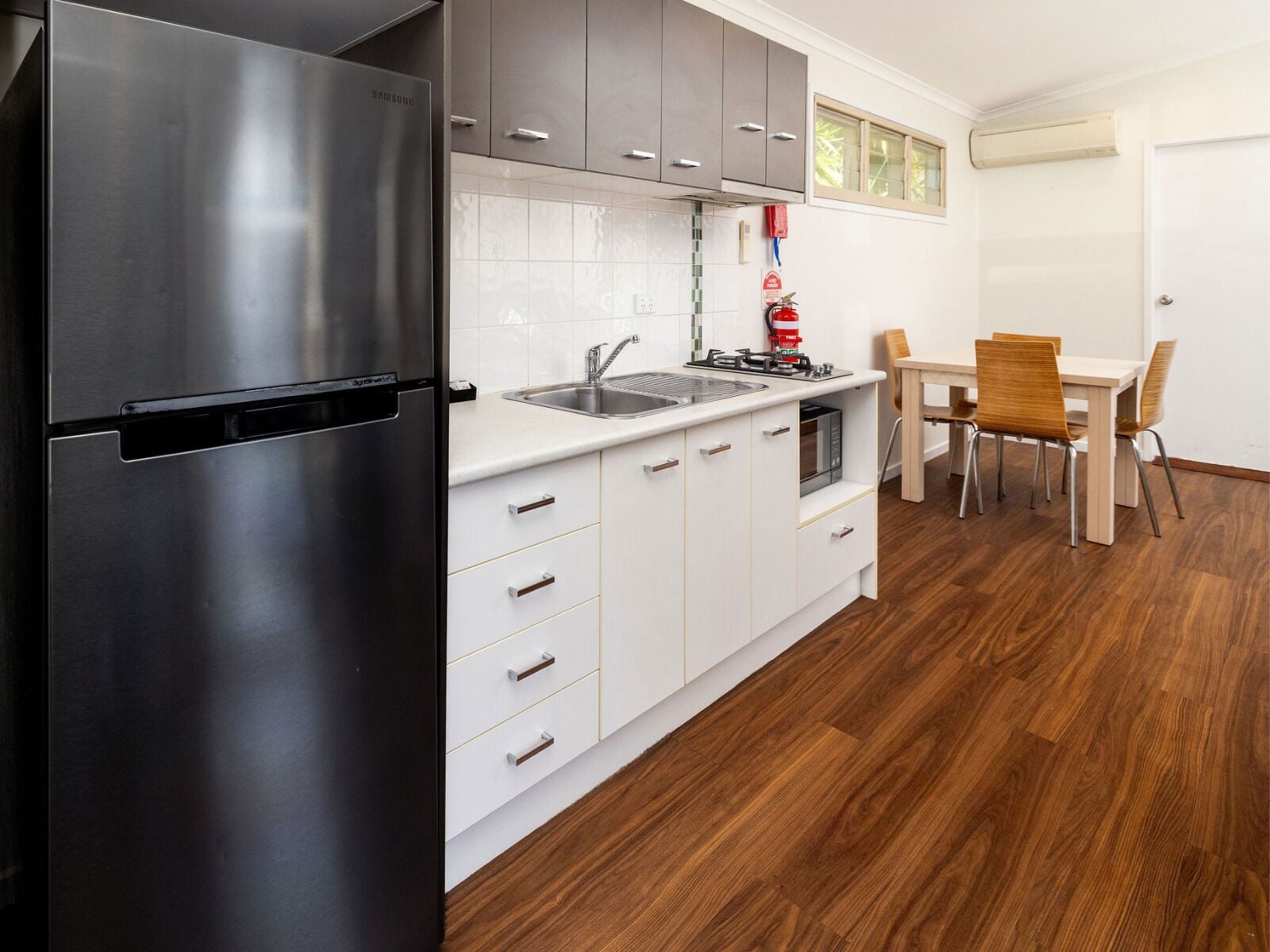 A modern kitchen with white cabinets, a stainless steel refrigerator, a microwave, and a wooden dining table with chairs.