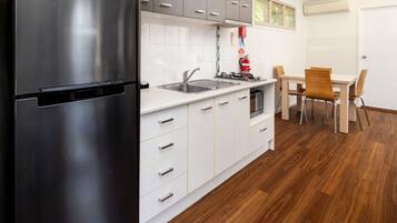 A modern kitchen with white cabinets, a stainless steel refrigerator, a microwave, and a wooden dining table with chairs.