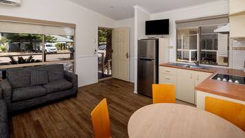 A compact kitchen with a built-in refrigerator, a dining area with a round table and chairs, and a sofa in a living area with a view of the street.