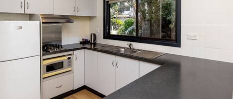 A compact kitchen with white cabinets, a black countertop, a built-in oven, and a window with a view of greenery outside.